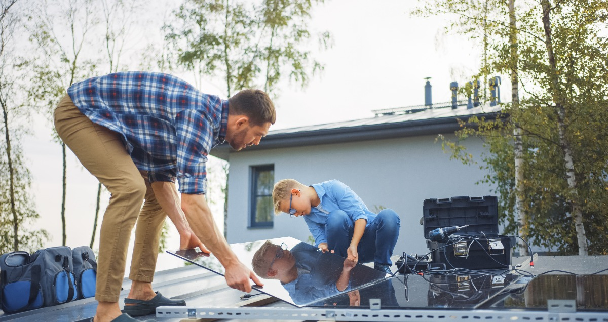 Parent and child install solar panels on roof of home