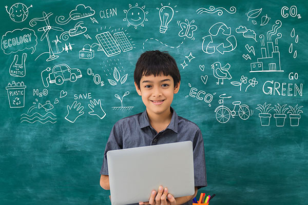 Child holding laptop in front of green chalk board