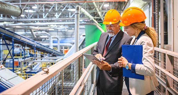 Man and woman in hard hat and safety vest in industrial building