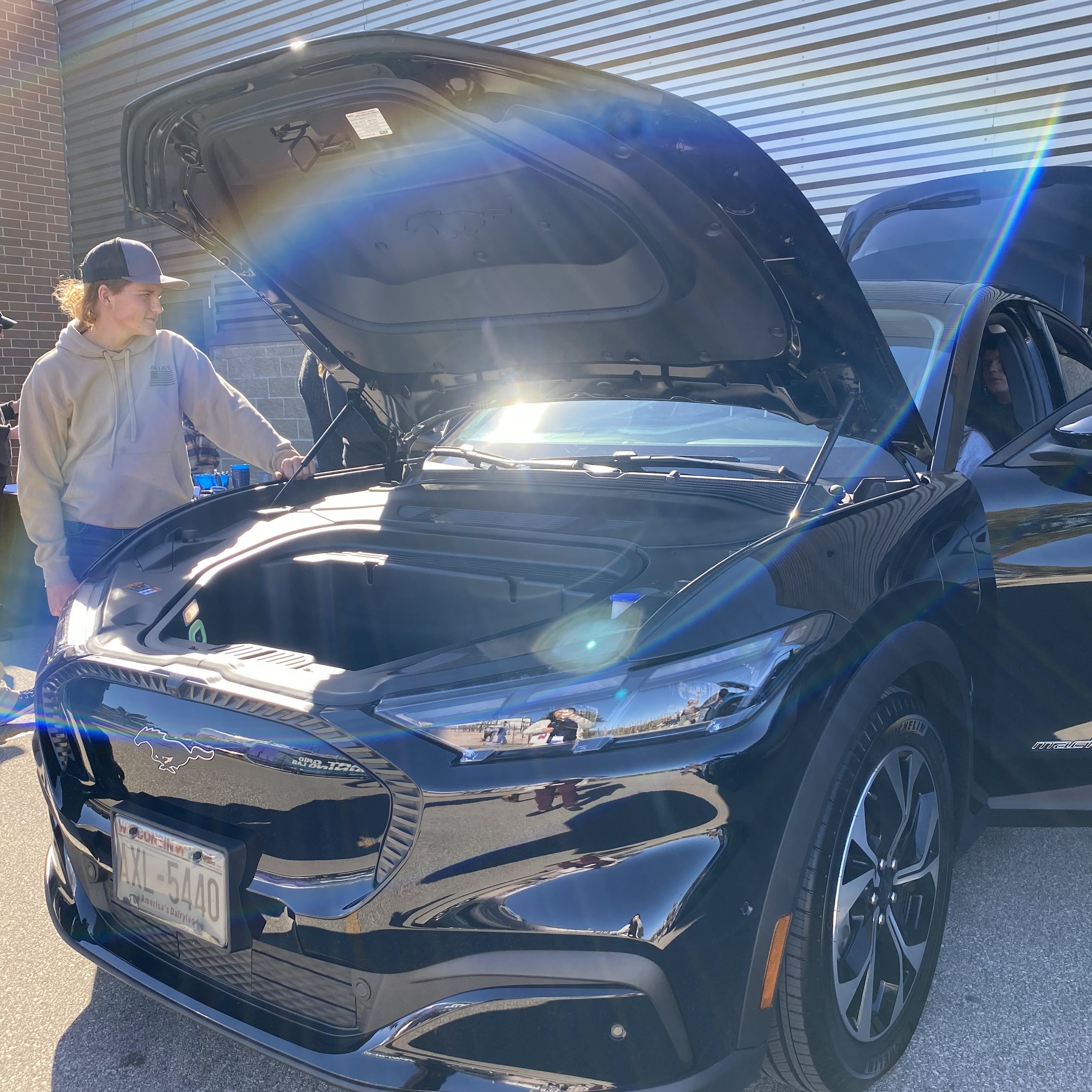 Student observing an electric vehicle with its hood popped open